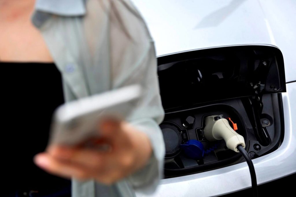 Femme devant une voiture électrique qui se charge