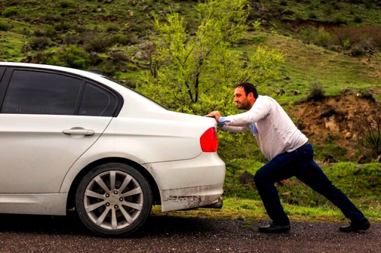Homme qui pousse une voiture en panne