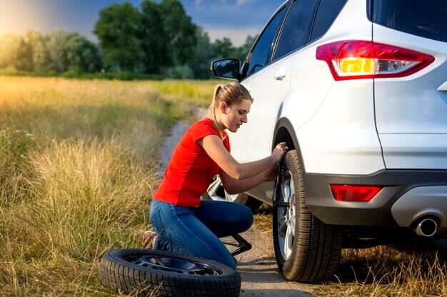 Jeune femme changeant une roue de voiture